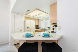 Kitchen with a breakfast bar, a peninsula, light countertops, white appliances, and light wood finish cabinets