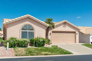 Mediterranean / spanish-style house featuring a garage, stucco siding, driveway, a tile roof, and a front lawn