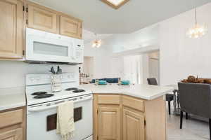 Kitchen with white appliances, light wood finish cabinets, a peninsula, and light countertops