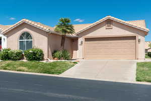 Mediterranean / spanish-style house featuring stucco siding, an attached garage, driveway, a front lawn, and a tiled roof