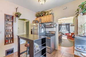 Kitchen featuring arched walkways, stainless steel appliances, light wood finish cabinetry, open shelves, and light tile patterned flooring