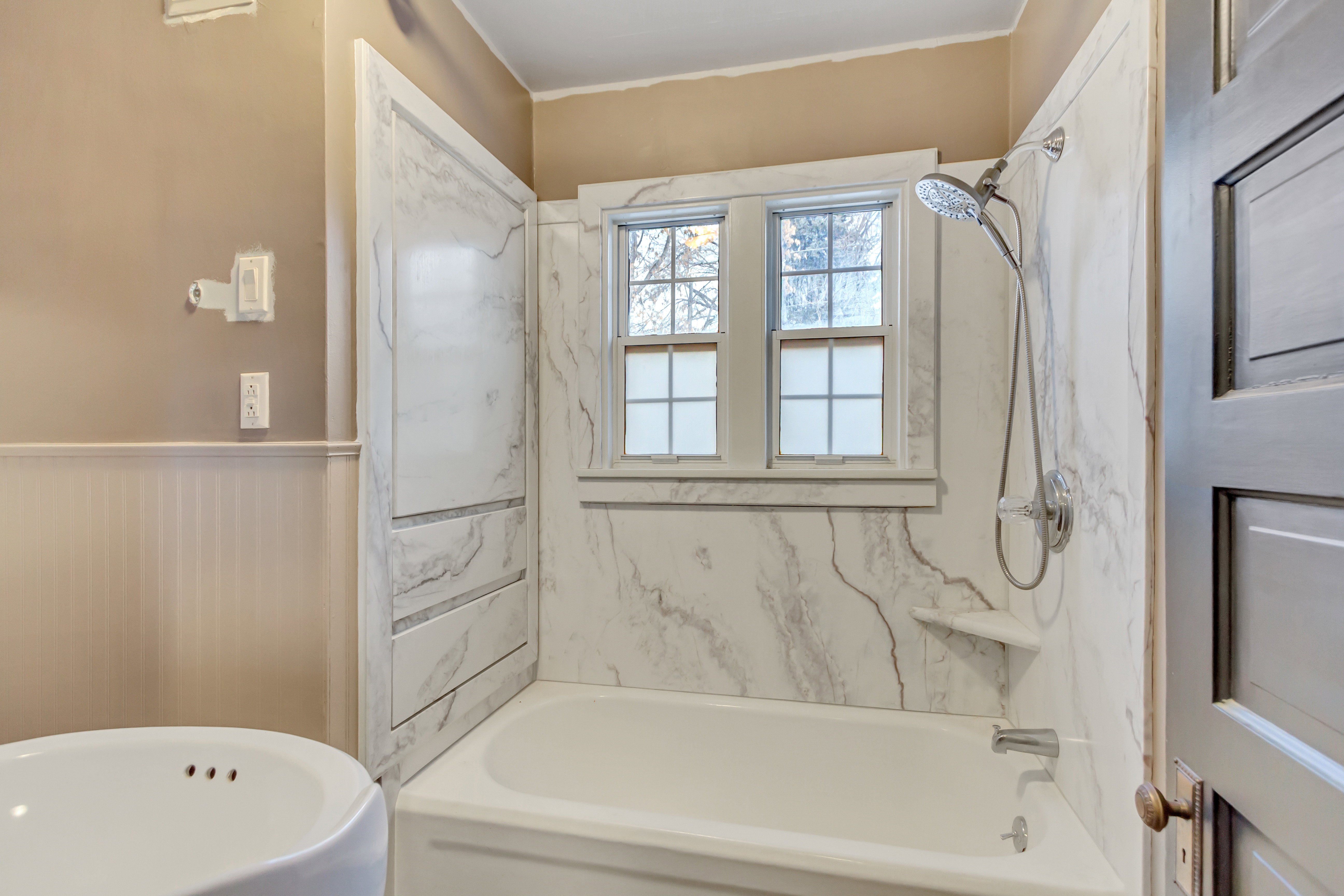Full bathroom featuring a combined bath / shower with marble appearance, a wainscoted wall, and ornamental molding