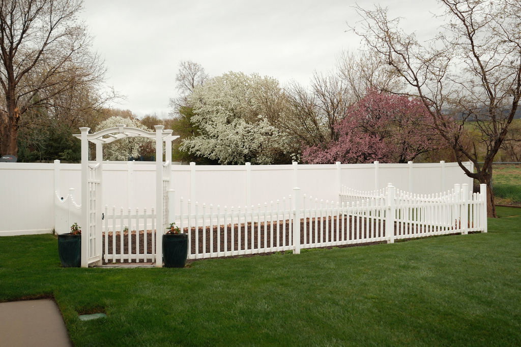 Expansive lawn area featuring a white vinyl privacy fence and a charming white picket fence enclosure