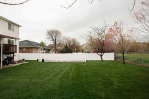 Expansive green lawn with a white vinyl fence and mature trees