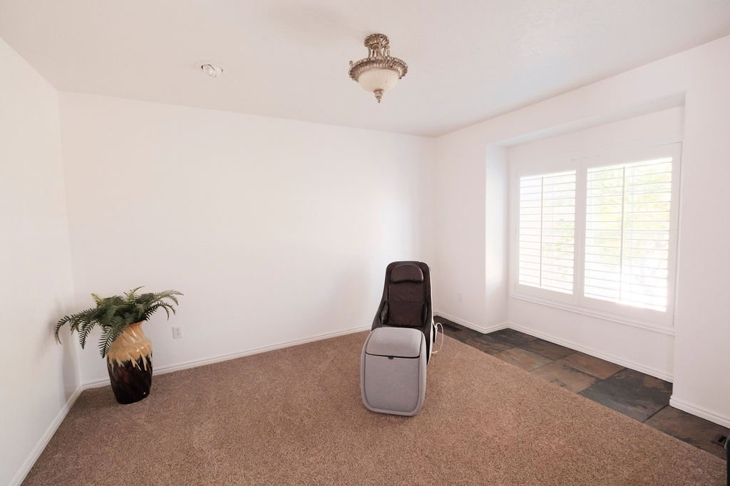 Room featuring white walls, carpet flooring, recessed lighting, a decorative ceiling fixture, and a window with white louvered shutters and a stone-finish flooring accent