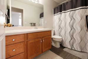 Bathroom featuring a wood-finish vanity with an integrated sink, a neutral-toned countertop, a large wall-mounted mirror, and wood-finish flooring