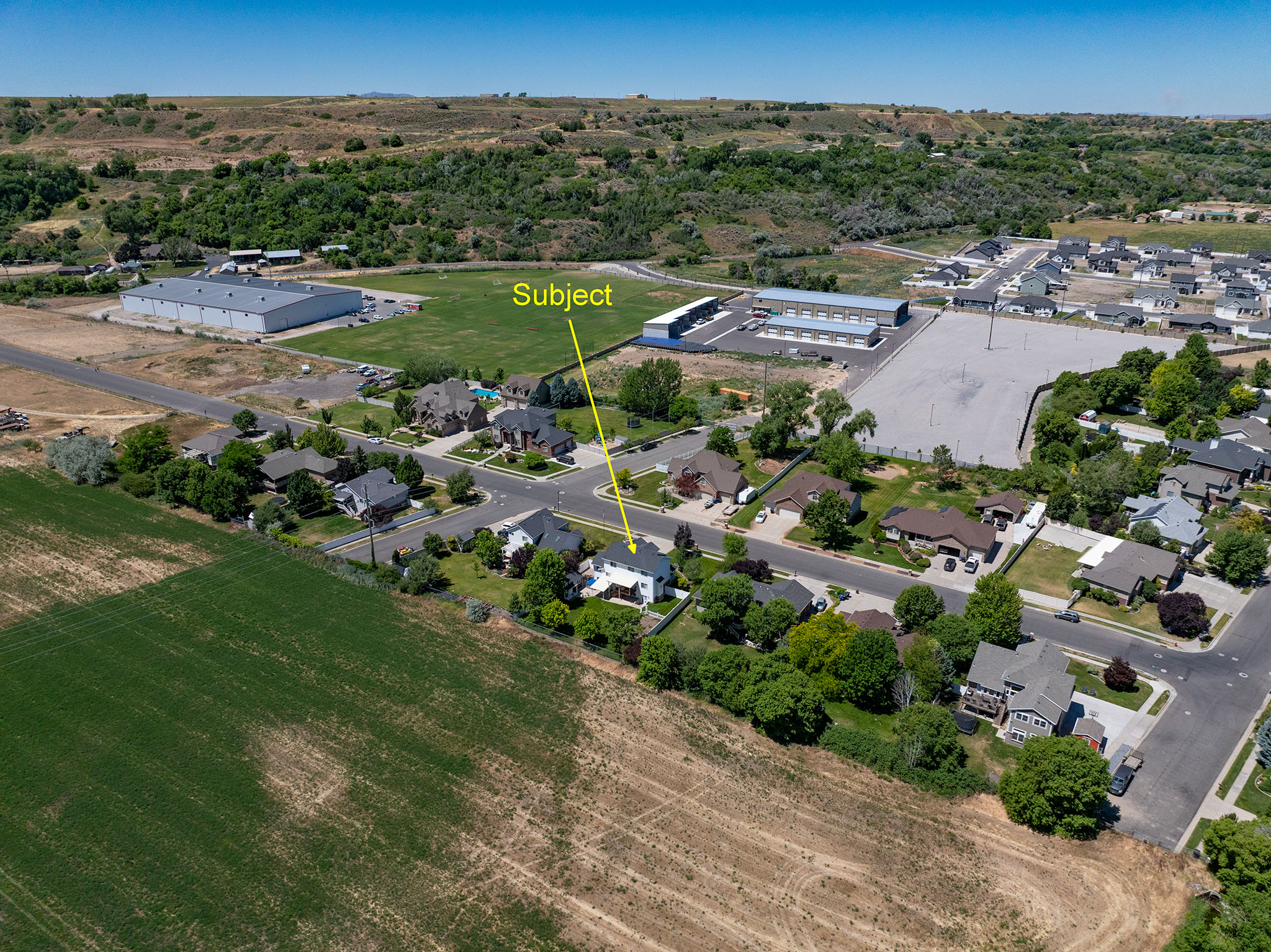 Aerial perspective highlighting residential properties bordered by agricultural fields and distant hills