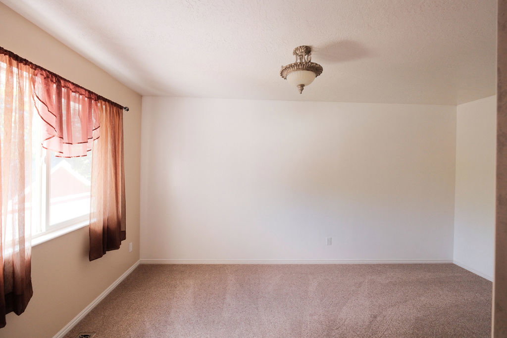 Spacious room featuring neutral carpeting, a large window, and an ornate ceiling light fixture