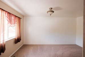 Spacious room featuring neutral carpeting, a large window, and an ornate ceiling light fixture
