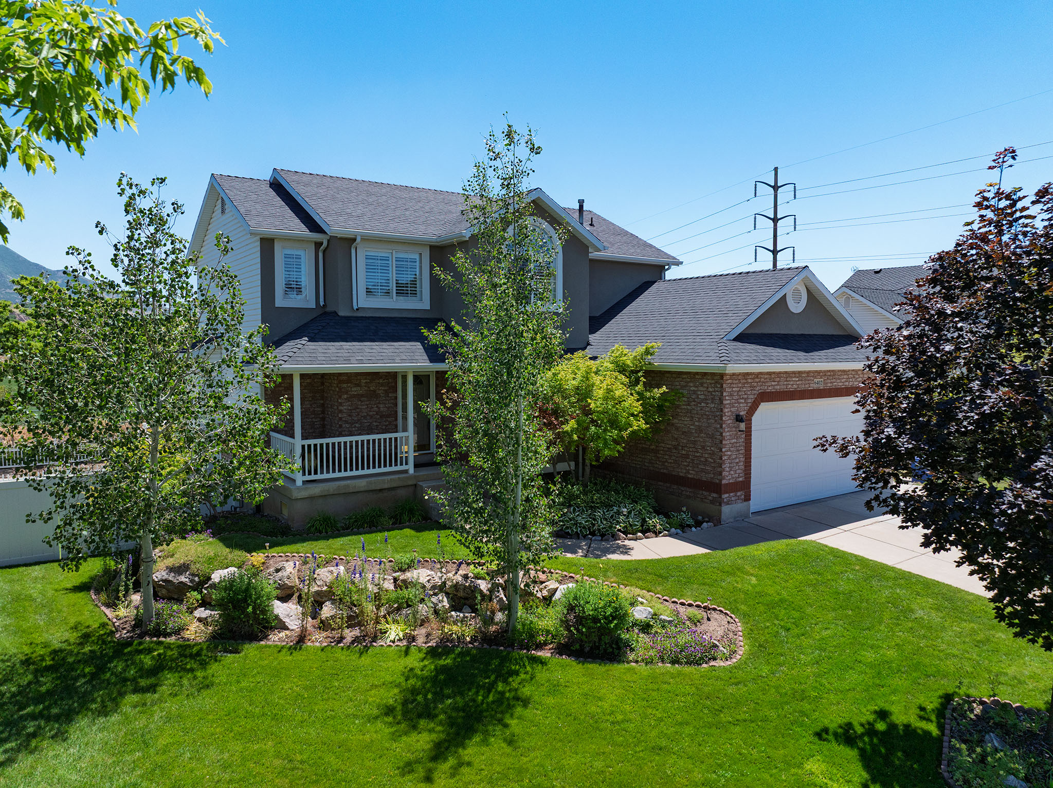 Two-story residence featuring a covered front porch with white railing, brick and siding exterior finishes, an attached garage with a white door, and a landscaped front yard with a rock garden