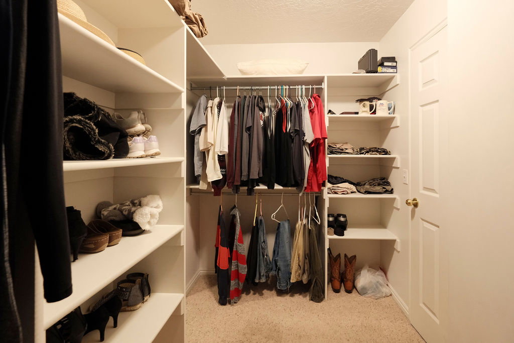 Walk-in closet featuring built-in shelving, multiple hanging rods, corner shelving units, and neutral carpeting