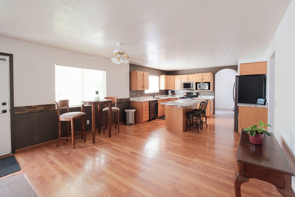 Open-concept kitchen and dining area featuring wood-finish flooring, light wood cabinetry, stone countertops, and a full suite of appliances