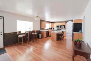 Open-concept kitchen and dining area featuring wood-finish flooring, light wood cabinetry, stone countertops, and a full suite of appliances