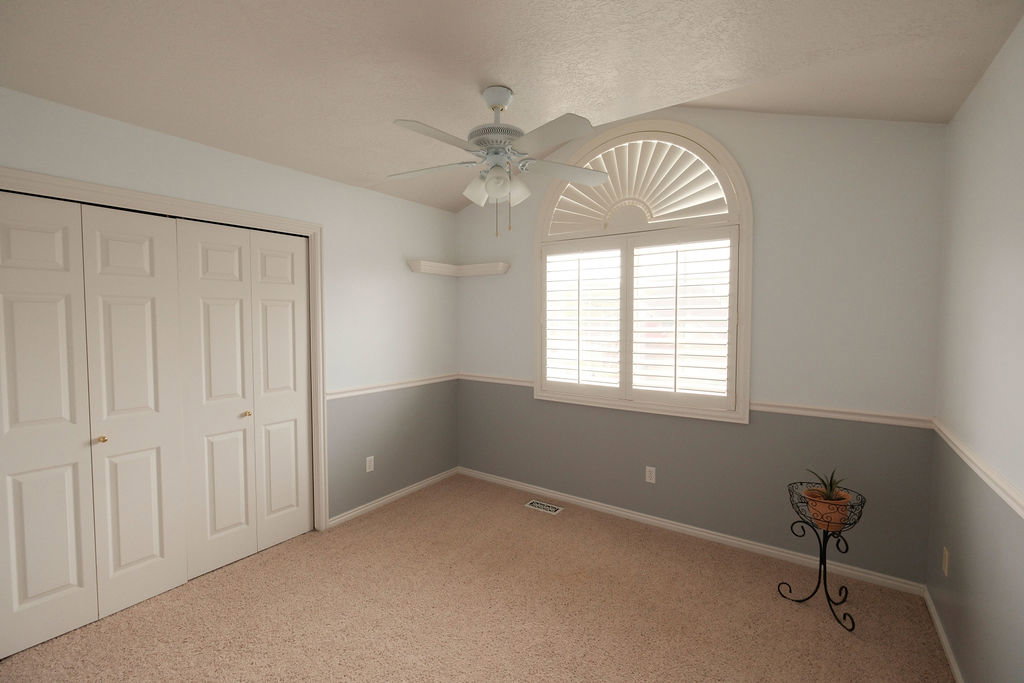 Room featuring an arched window with plantation shutters, vaulted ceiling, and ceiling fan