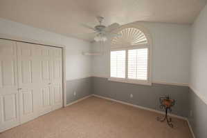 Room featuring an arched window with plantation shutters, vaulted ceiling, and ceiling fan