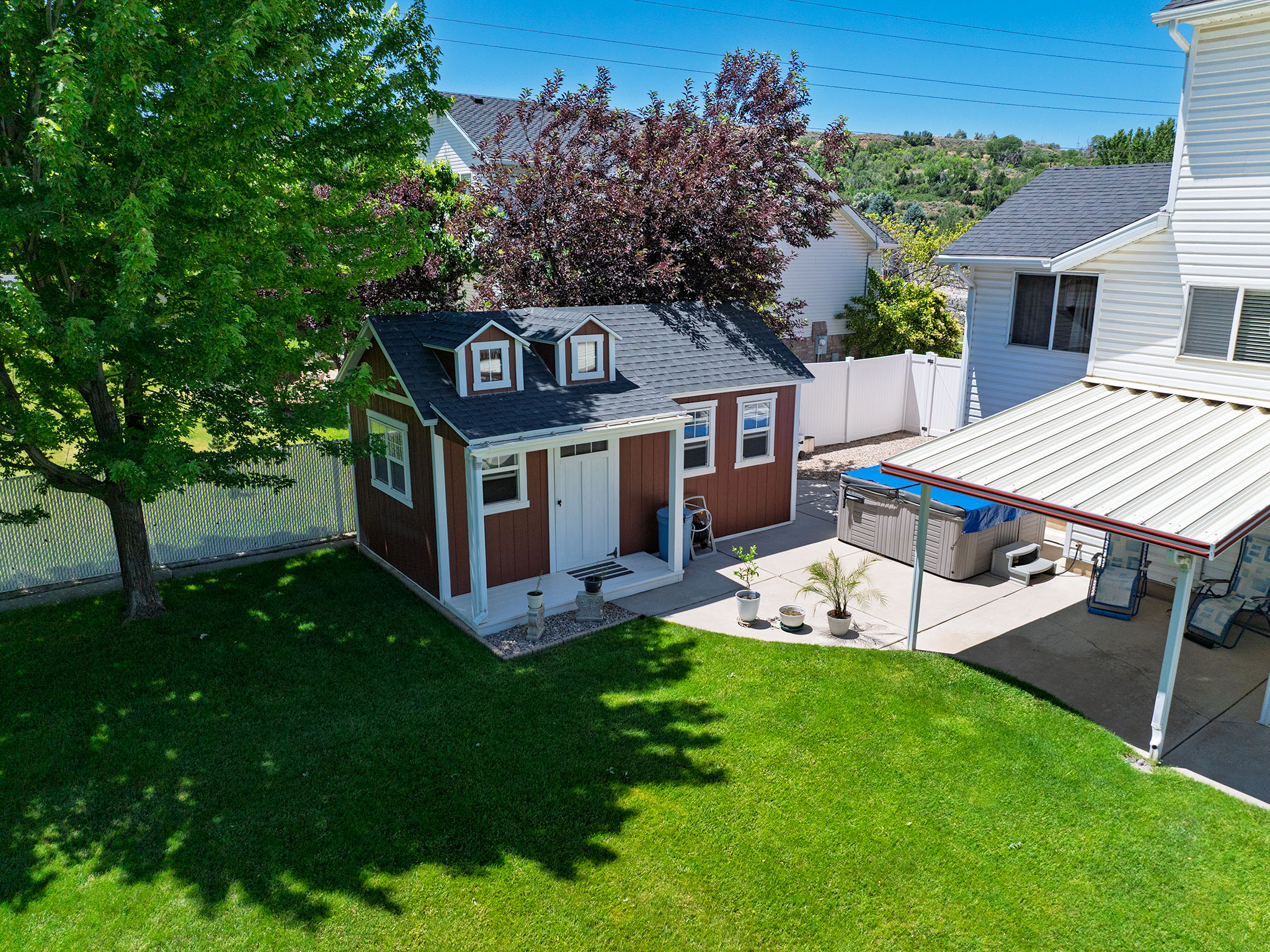 Expansive backyard featuring a manicured lawn, a detached storage shed with dormers, and a covered patio area