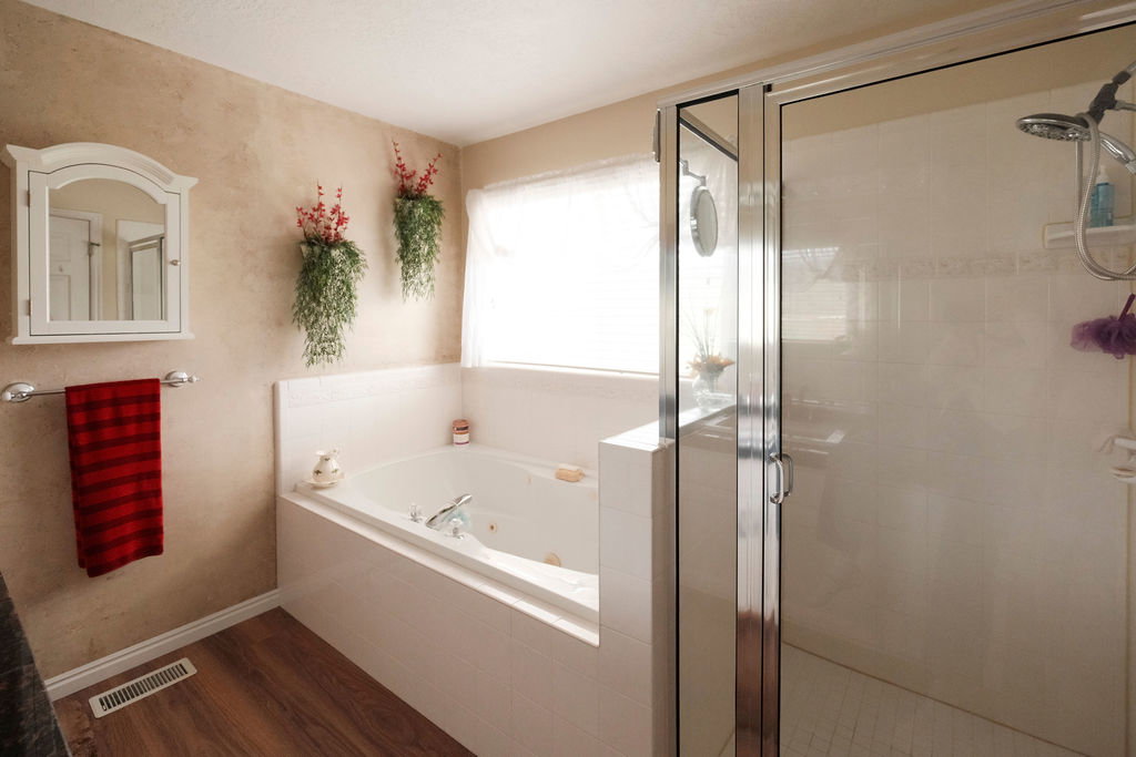 Bathroom featuring a built-in jetted tub, a glass-enclosed shower, wood-finish flooring, a wall-mounted medicine cabinet, and a chrome towel bar