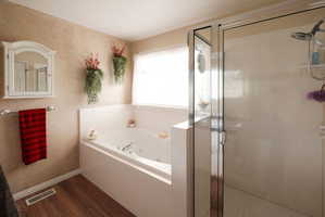 Bathroom featuring a built-in jetted tub, a glass-enclosed shower, wood-finish flooring, a wall-mounted medicine cabinet, and a chrome towel bar
