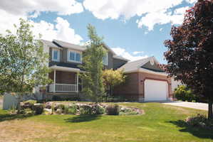 Two-story residence featuring a brick and siding exterior, a covered front porch with white railings, a two-car garage, and mature landscaping