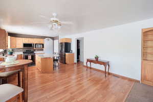 Open-concept layout featuring wood-finish flooring, a kitchen island with seating, natural wood cabinetry, and built-in shelving
