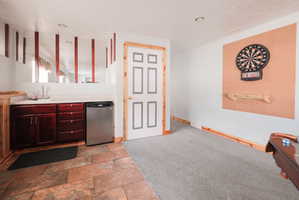 Lower-level recreation space featuring a wet bar with dark wood cabinetry, a built-in stainless steel beverage refrigerator, and stone tile flooring