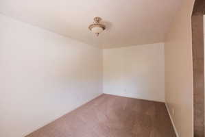 Carpeted room with a textured ceiling, a decorative semi-flush mount light fixture, and neutral-toned walls