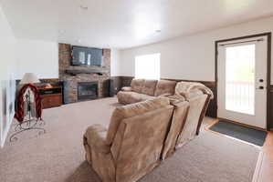 Living area featuring a stone accent wall with a built-in fireplace and mantel, recessed lighting, carpet flooring, a white-framed glass door, and a window
