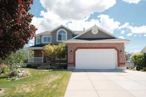 Stucco and brick facade with an arched garage door, a prominent front porch with white railings, and mature landscaping
