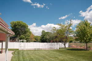 Expansive backyard featuring a manicured lawn, a white vinyl privacy fence, and mature trees