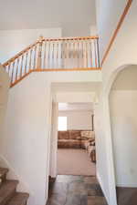 Two-story entryway featuring a natural wood-finish staircase and second-level balustrade, high ceilings, arched doorway, and stone-finish flooring