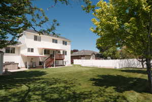 Expansive backyard featuring a manicured lawn, a full white privacy fence, mature trees, and a concrete patio