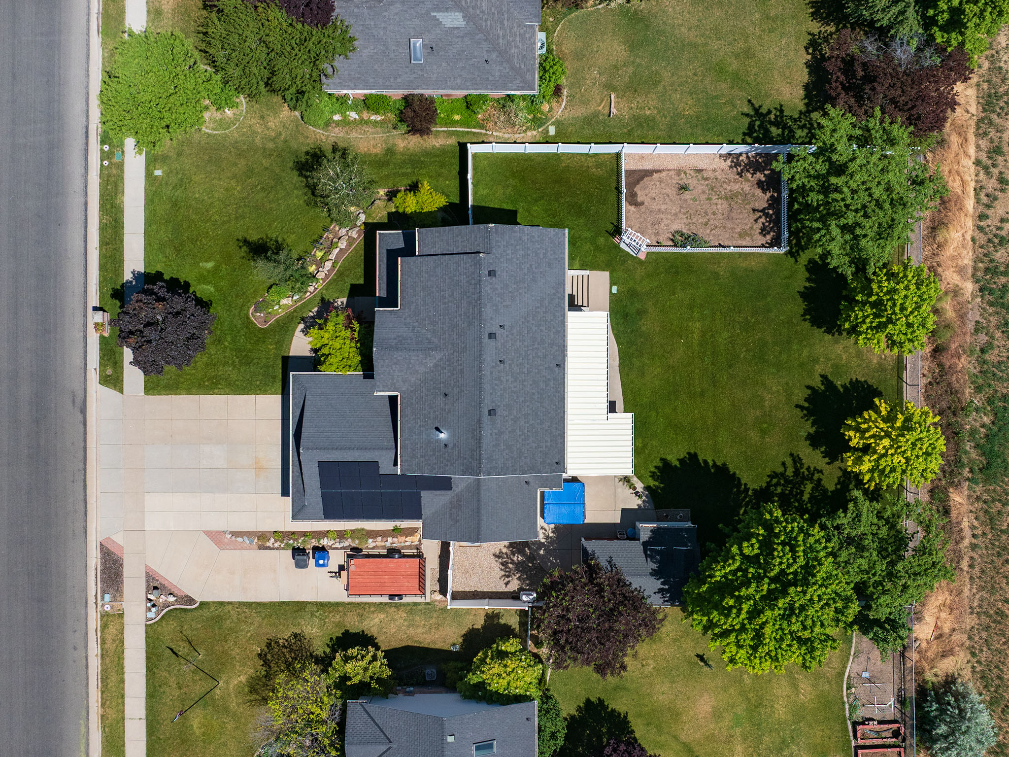 Expansive property featuring a paved driveway, a verdant lawn, mature trees, and a white fence enclosing a garden area