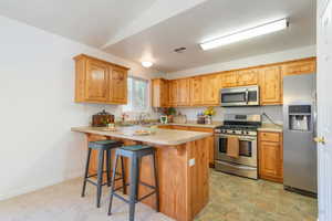 Kitchen featuring stainless steel appliances, light countertops, a kitchen breakfast bar, and a peninsula
