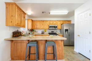 Kitchen with light countertops, stainless steel appliances, a peninsula, a kitchen breakfast bar, and light wood finish cabinets