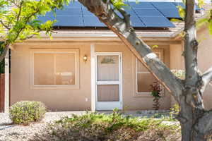 View of exterior entry with stucco siding and roof mounted solar panels