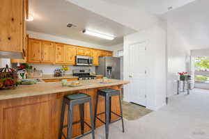 Kitchen with light countertops, a peninsula, a breakfast bar, light carpet, and stainless steel appliances