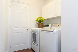 Laundry area featuring washer and clothes dryer, cabinet space, and dark wood finished floors