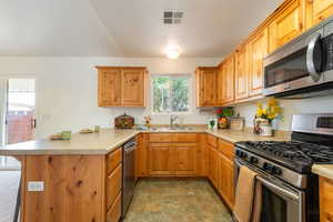 Kitchen featuring stainless steel appliances, a peninsula, light countertops, stone finish floors, and wood finish cabinets