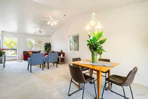 Dining space featuring light colored carpet, vaulted ceiling, suspended lighting, and ceiling fan