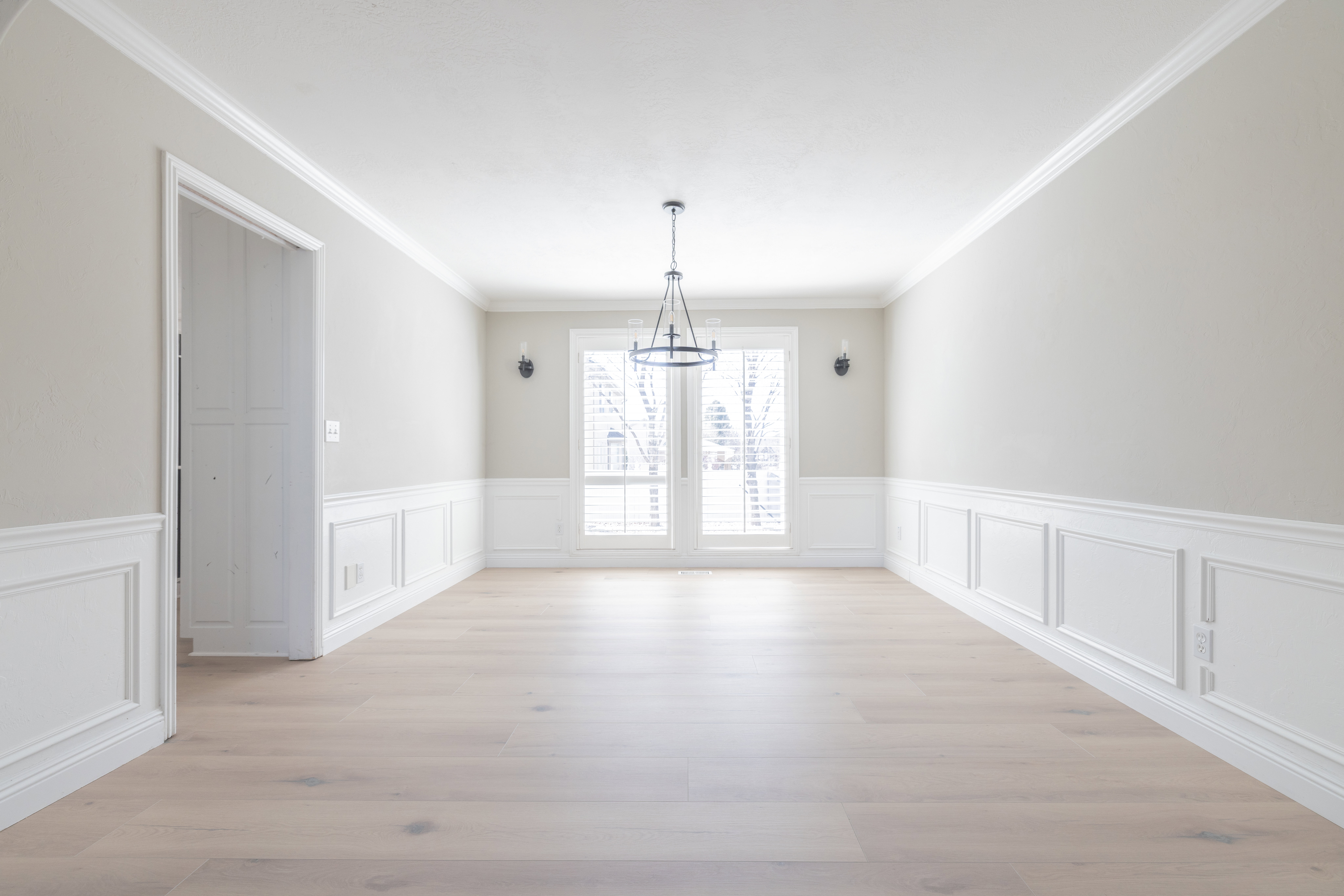 Unfurnished dining area with wainscoting, a decorative wall, crown molding, light wood finished floors, and suspended lighting