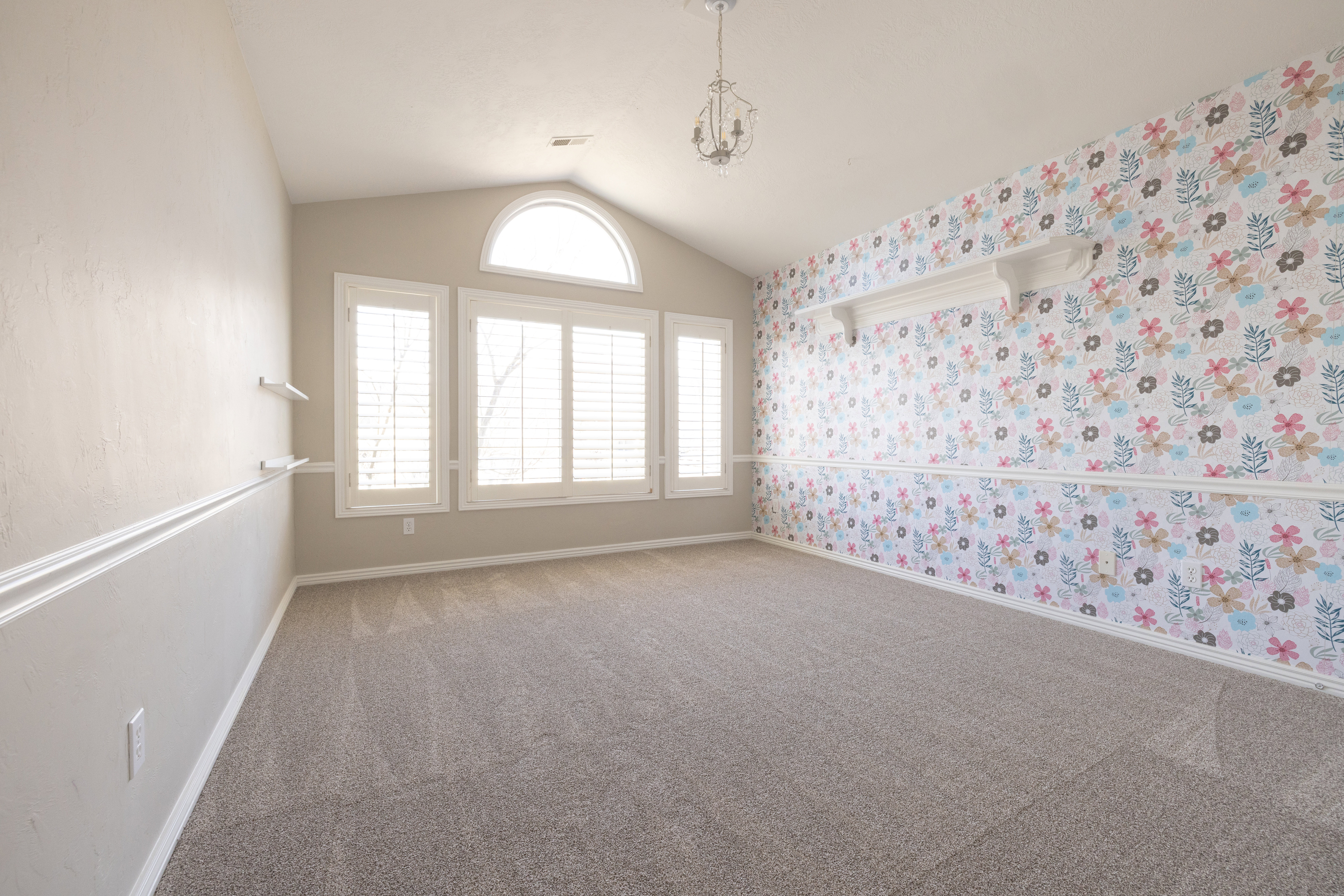 Carpeted spare room with wallpapered walls and a chandelier