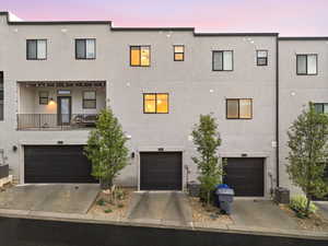 View of front facade featuring an attached garage, a balcony, stucco siding, and concrete driveway