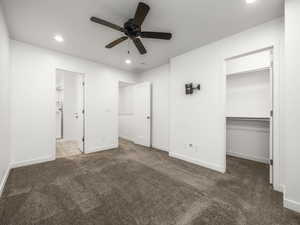 Unfurnished bedroom featuring a walk in closet, dark carpet, recessed lighting, and a ceiling fan