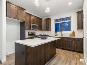 Kitchen with dark wood finish cabinetry, stainless steel appliances, light wood-style floors, a kitchen island, and decorative light fixtures