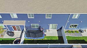 Rear view of house featuring a patio area, a shingled roof, a yard, and a trampoline