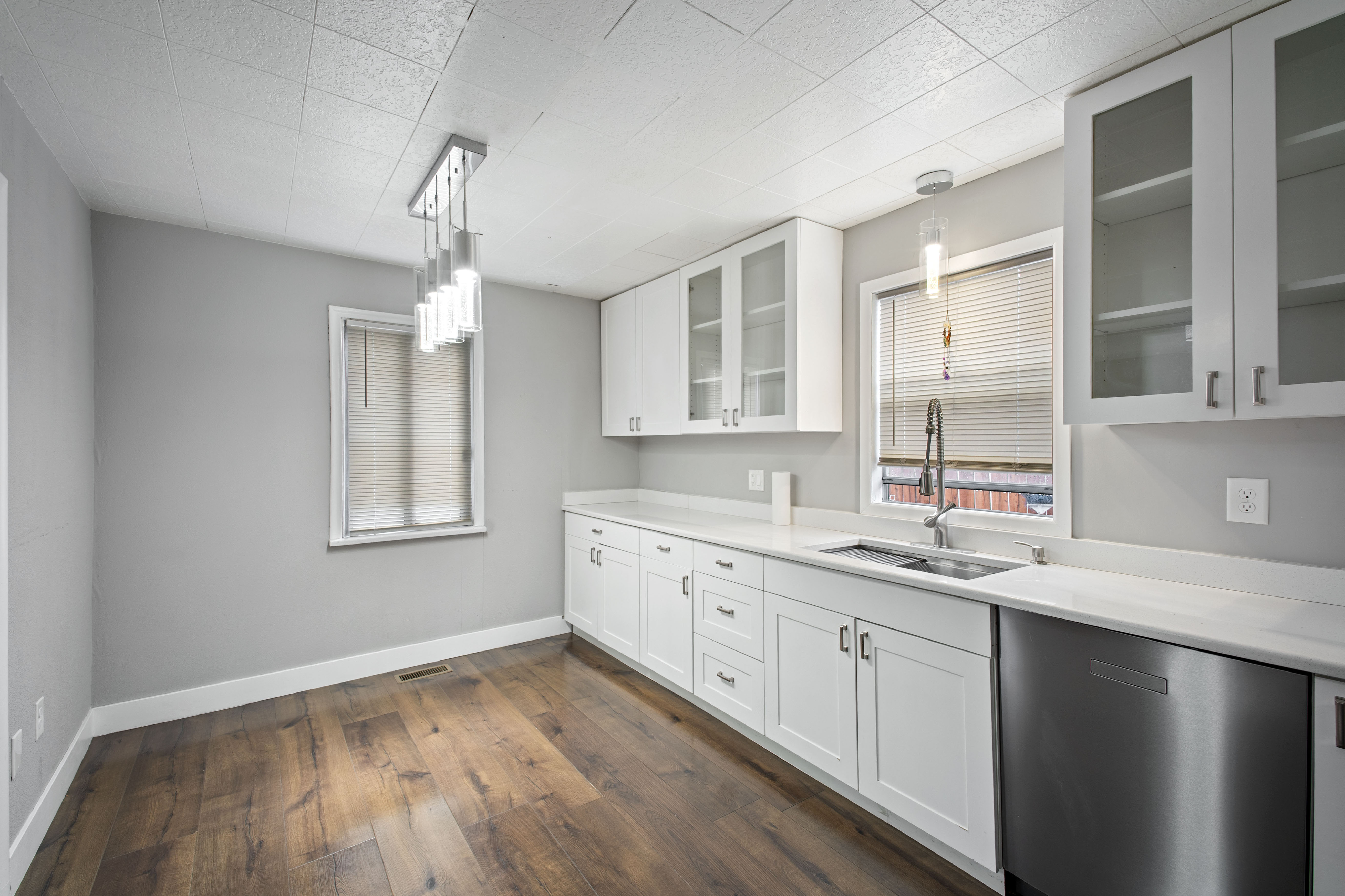 Kitchen featuring decorative light fixtures, dishwasher, white cabinetry, dark wood-style floors, and glass fronted cabinets