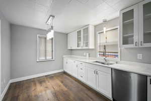 Kitchen featuring decorative light fixtures, dishwasher, white cabinetry, dark wood-style floors, and glass fronted cabinets