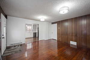 Unfurnished living room with wood walls, dark wood finished floors, and a textured ceiling