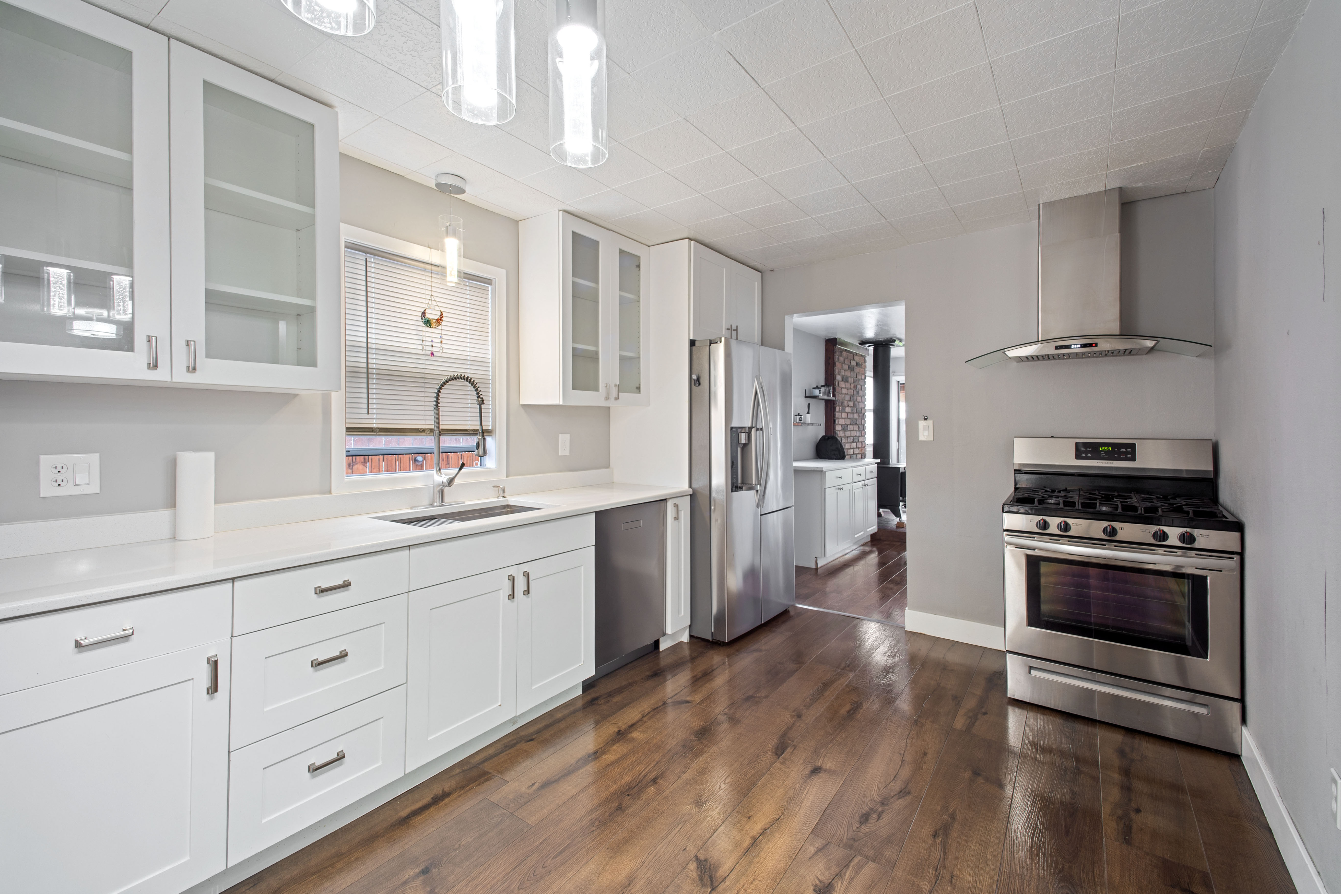Kitchen featuring stainless steel appliances, white cabinetry, glass insert cabinets, dark wood finished floors, and decorative light fixtures