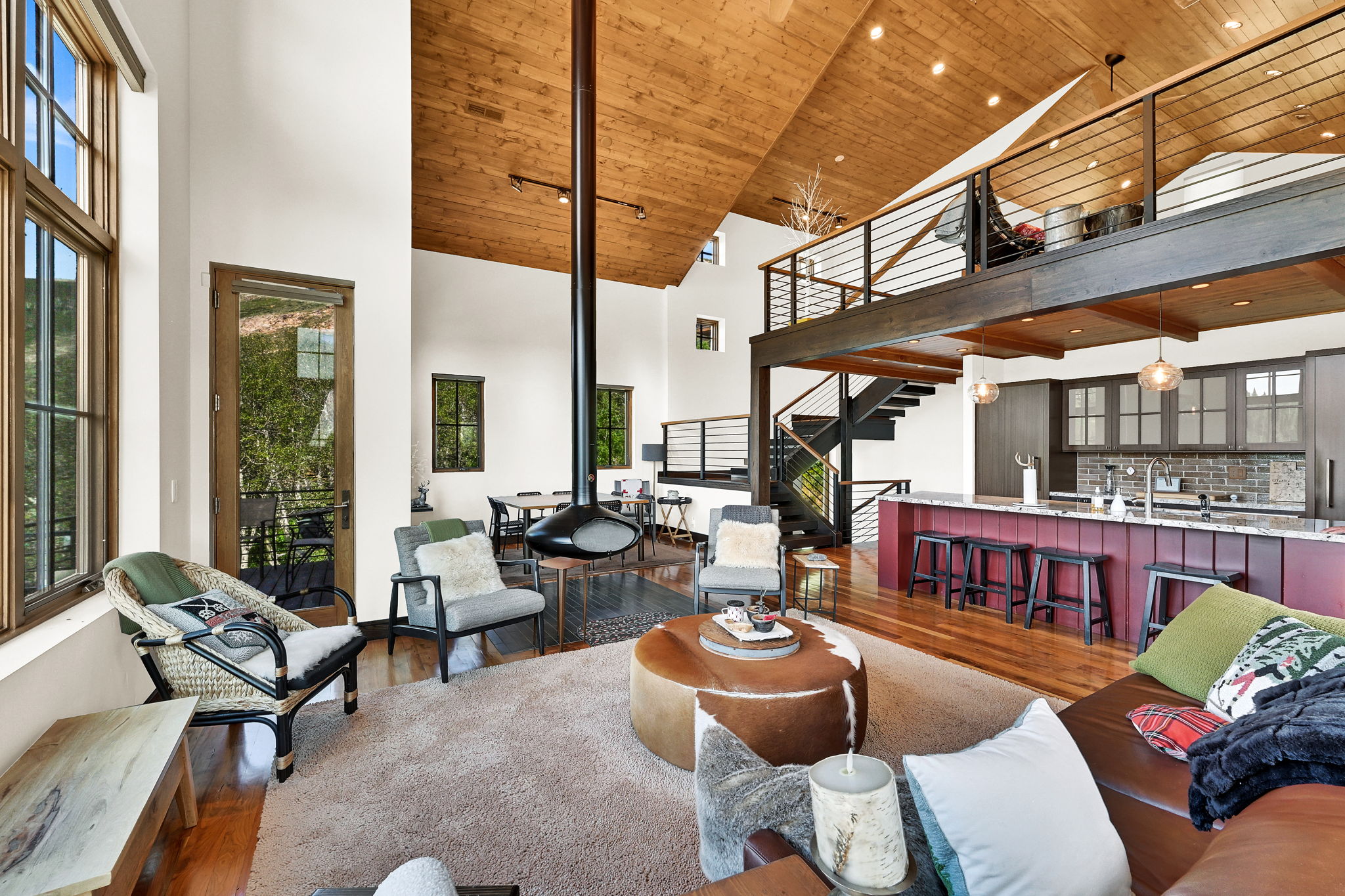 Living area featuring a vaulted wood-paneled ceiling, suspended fireplace, and large picture windows